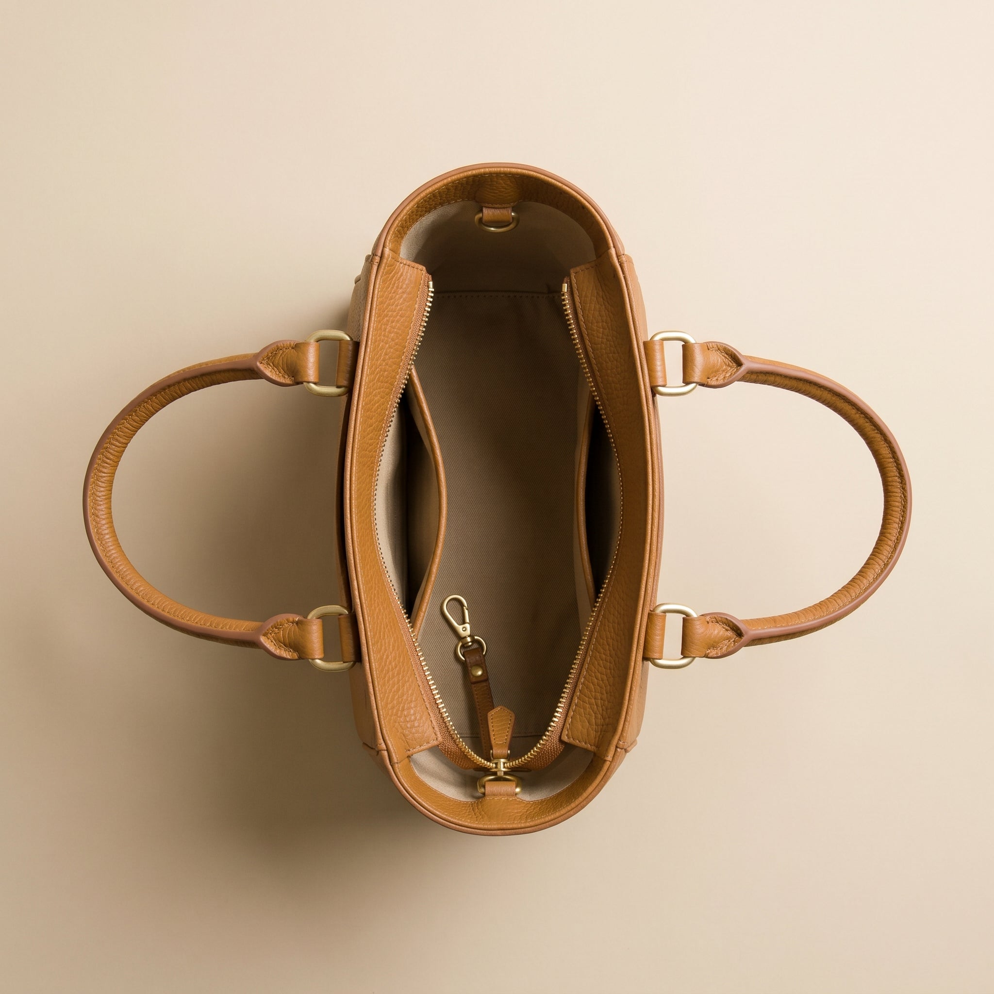 Brown leather handbag with gold hardware on a beige background